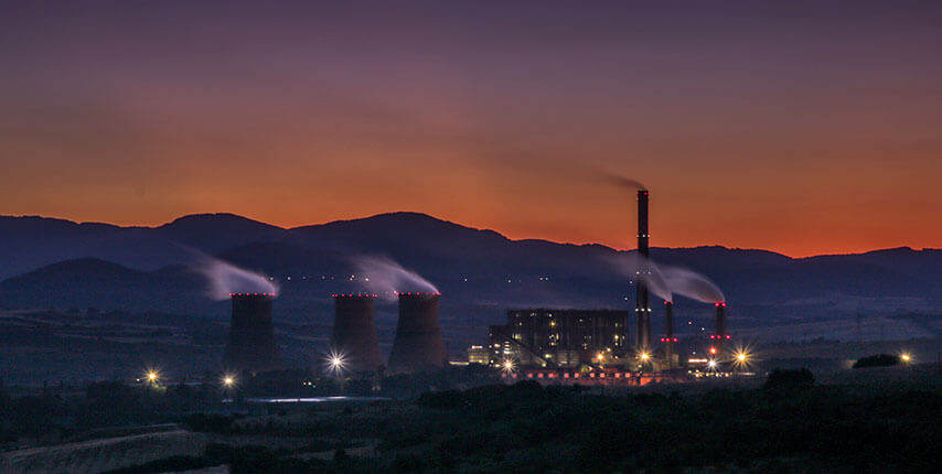 Foto de uma industria de energia, com montanhas e por do sol atrás